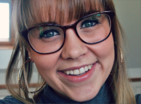 Girl with thick, brown, round glasses and full fringe smiling at the camera