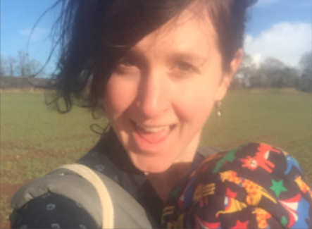 Woman with short dark hair smiling facing the camera, in a field