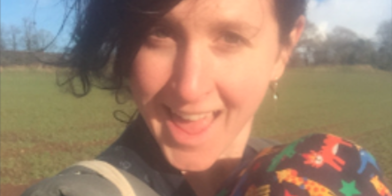 Woman with short dark hair smiling facing the camera, in a field