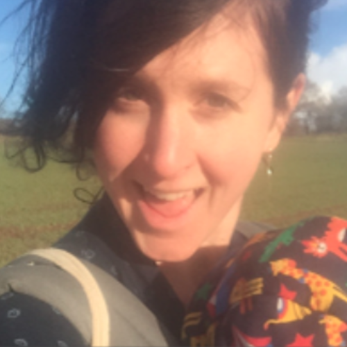 Woman with short dark hair smiling facing the camera, in a field