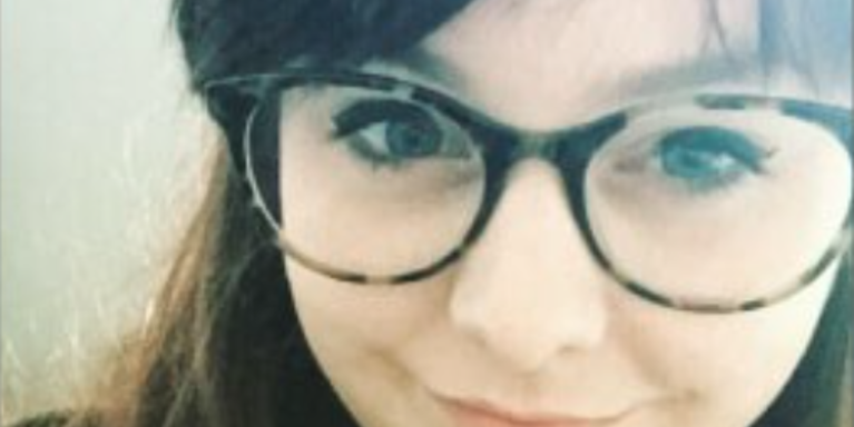 Young-looking woman wearing tortoise shell framed glasses, smiling at the camera
