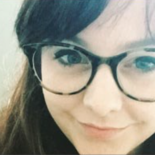 Young-looking woman wearing tortoise shell framed glasses, smiling at the camera