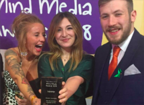two females and one male standing together, all smiling, with one female holding an award