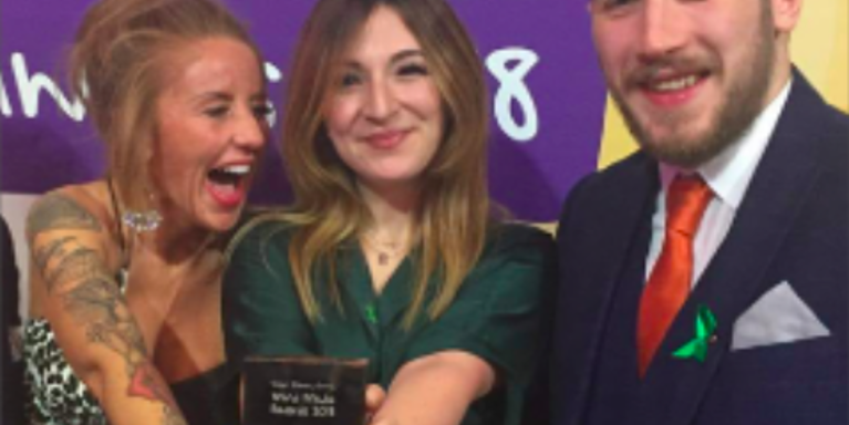 two females and one male standing together, all smiling, with one female holding an award