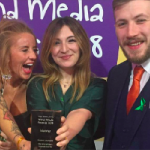 two females and one male standing together, all smiling, with one female holding an award