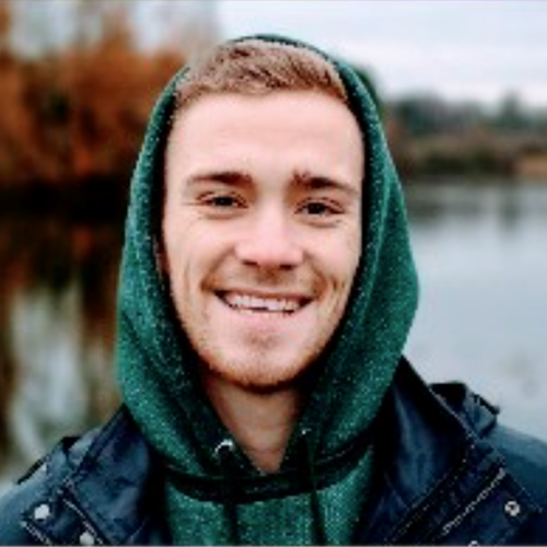 Male smiling with green hoodie on, with a lake behind him