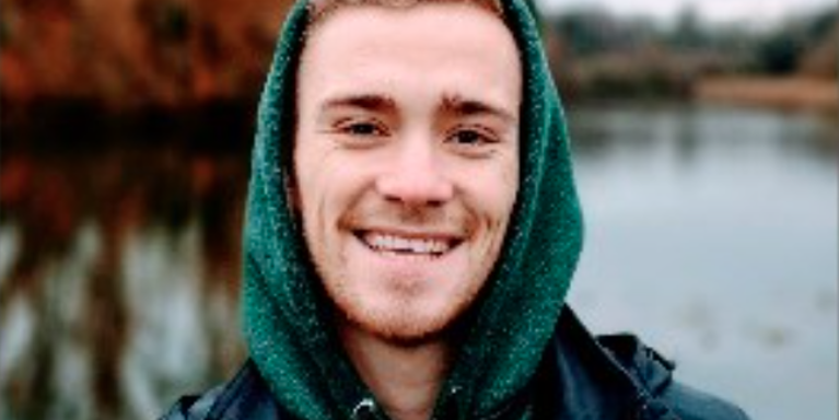 Male smiling with green hoodie on, with a lake behind him