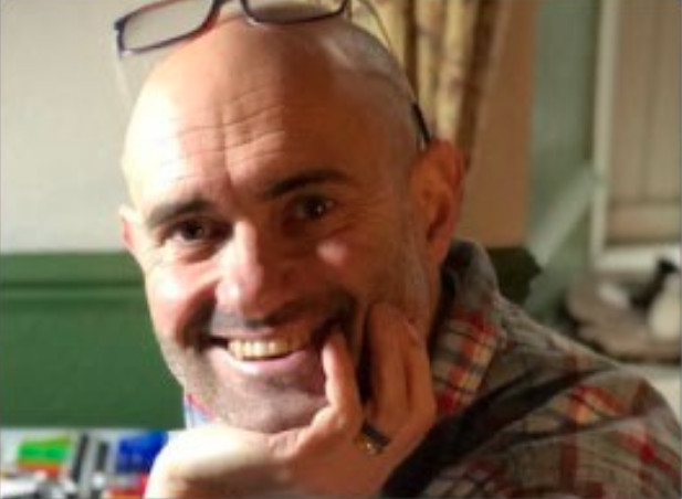 male smiling his his head in his hand and glasses on his head