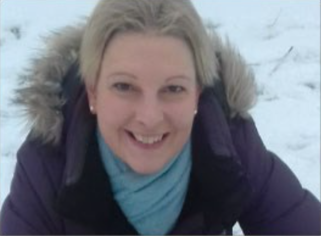 female smiling, snow on the ground wearing a coat with fur fringed hood