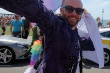 Male holding a flag with people and cars around him and an LGBT+ flag skirt