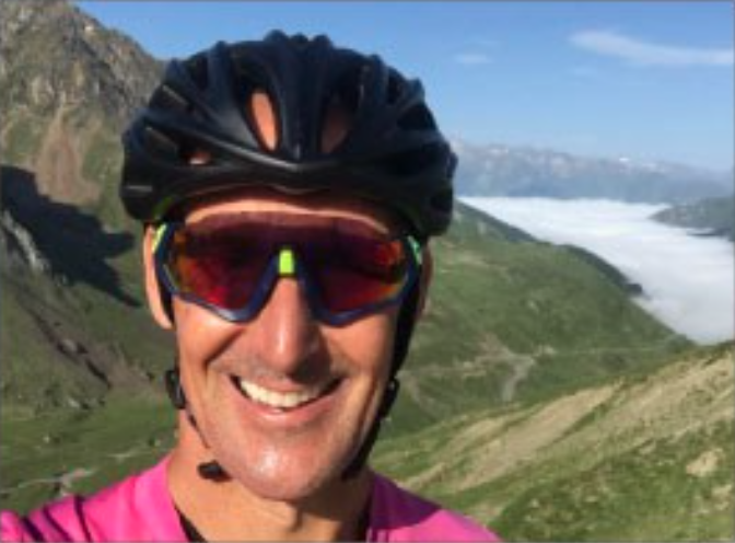 male wearing cycling helmet and sunglasses with a mountain terrain behind