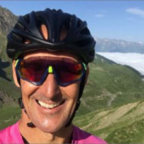 male wearing cycling helmet and sunglasses with a mountain terrain behind