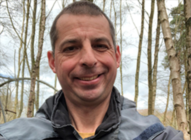 Male smiling with bare trees behind him