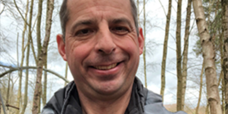 Male smiling with bare trees behind him