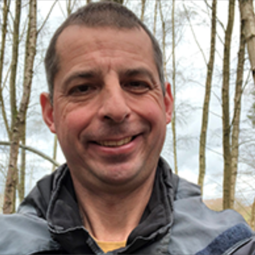 Male smiling with bare trees behind him