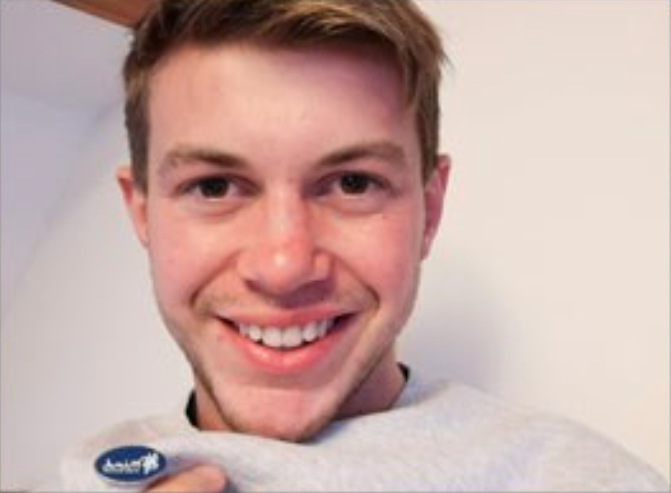 Male smiling holding a badge pinned to his jumper