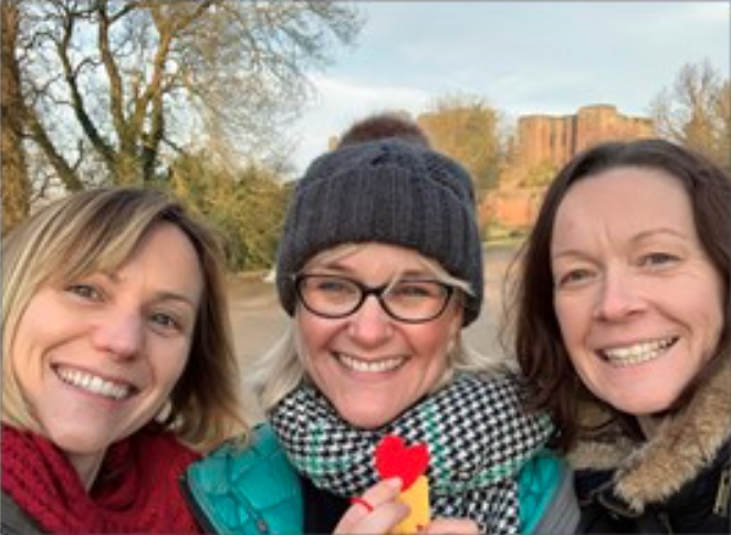 three females next next to each other wearing winter coats, hats and scarves, smiling