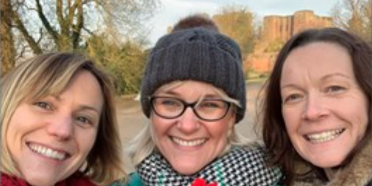 three females next next to each other wearing winter coats, hats and scarves, smiling