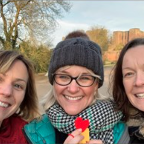 three females next next to each other wearing winter coats, hats and scarves, smiling