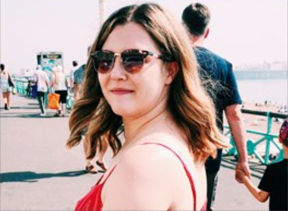 female turned to smile at camera with sunglasses on, standing in on a pier