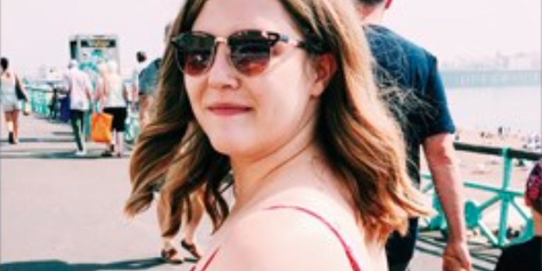 female turned to smile at camera with sunglasses on, standing in on a pier