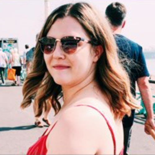 female turned to smile at camera with sunglasses on, standing in on a pier