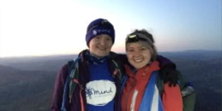 two females standing next to each other, arms on each others shoulders, on top of a mountain