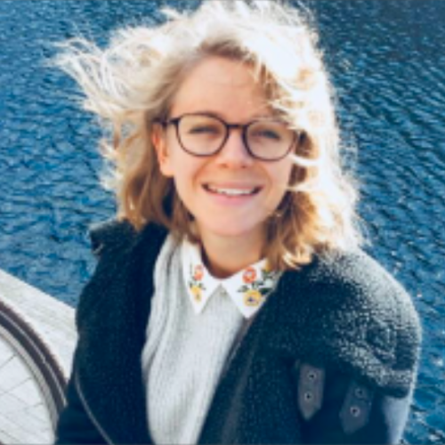 female smiling with her hair being flicked int he wind and is sitting in front of a body of water
