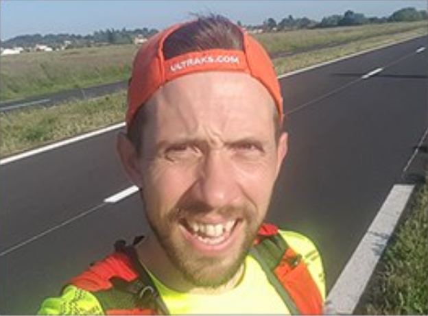 male wearing a orange cap and fluorescent yellow top, standing in front of the road