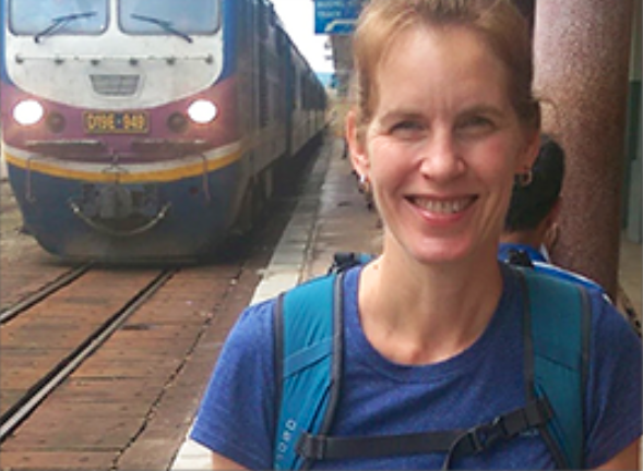 female on a station platform, standing with train approaching from behind