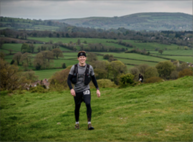 male in walking gear on a landscape with fields and hills