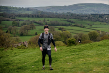 male in walking gear on a landscape with fields and hills