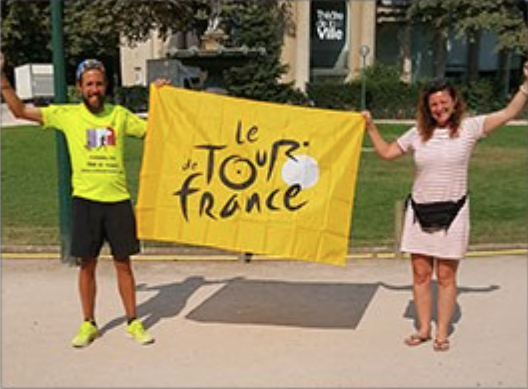 male and female holding a bright yellow flag with le tour de France on it
