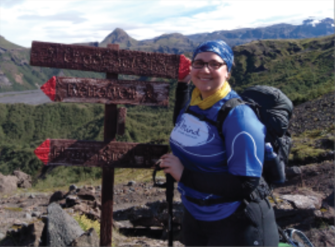 female smiling, standing next to wooden signs, on rocky terrain