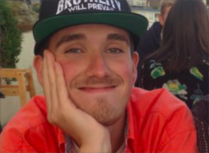 male smiling eith his head in his hands, wearing a snapback