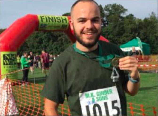 male holding a medal, standing in front of a race finishing line