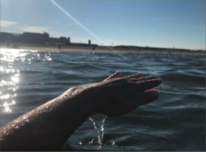 someone's hand lifted in the air, dripping with sea water, from the sea beneath it