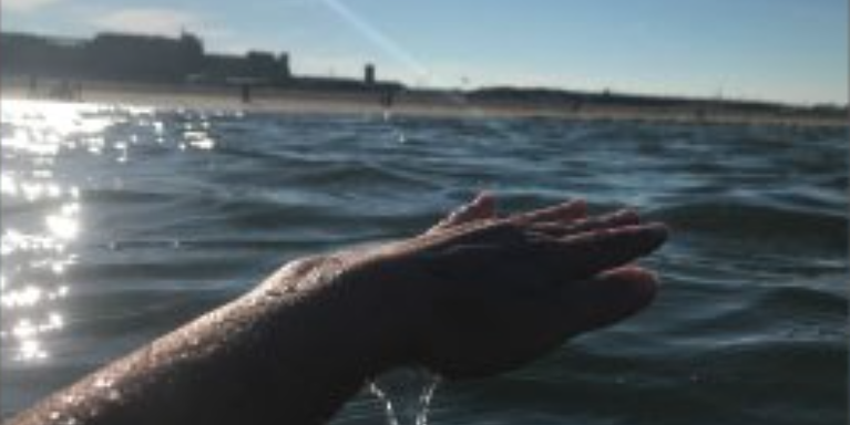 someone's hand lifted in the air, dripping with sea water, from the sea beneath it