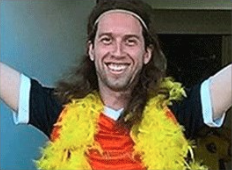 male smiling with his arms in the air, wearing a bright yellow boa feather