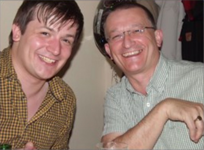 two males, one younger, one older, sitting together smiling