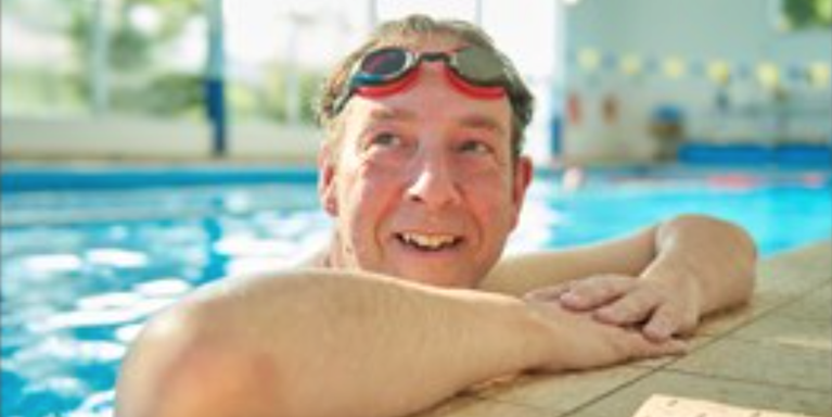 male wearing goggles leaning on the side of the swimming pool he is in