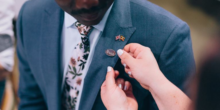 A man is having a Mind pin badge attached to his suit at a wedding