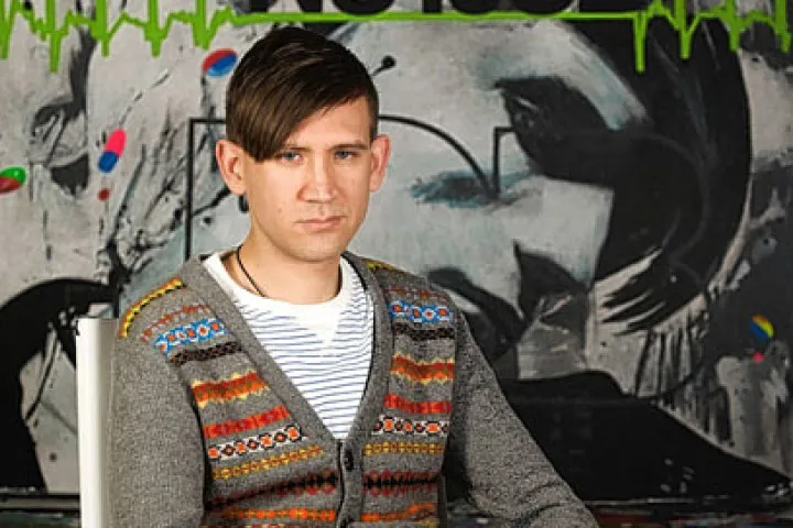 Stuart Semple sitting in front of artwork on wall