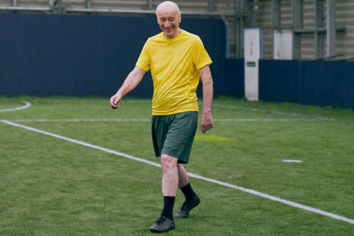 Man in yellow t-shirt walking on football pitch smiling Man in yellow t-shirt walking on football pitch smiling