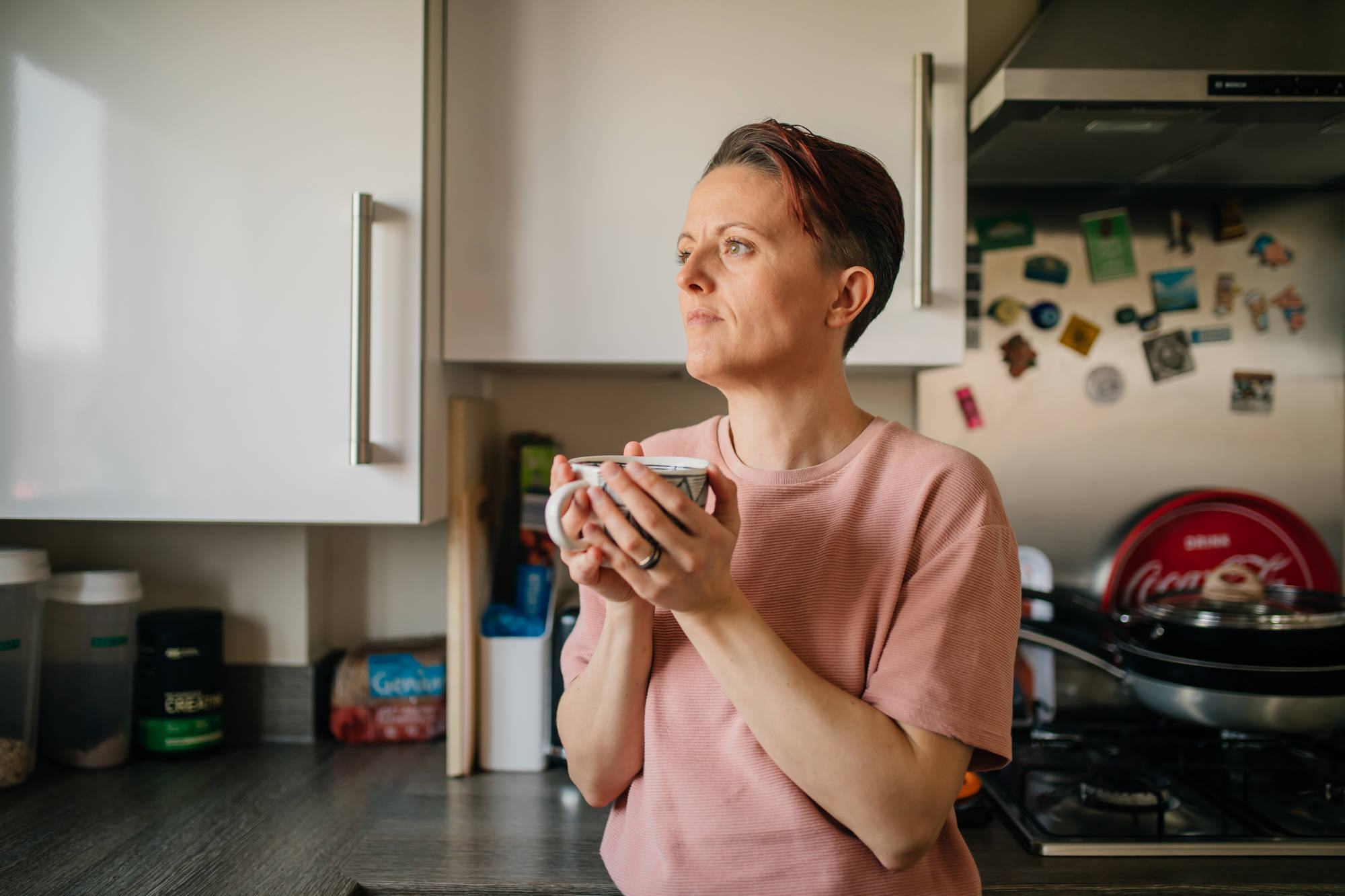 Woman leaning against kitchen counter top holding mug 