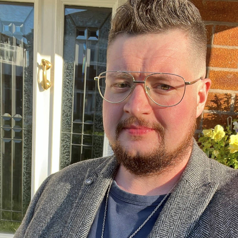 Person with glasses wearing a grey blazer and looking at the camera