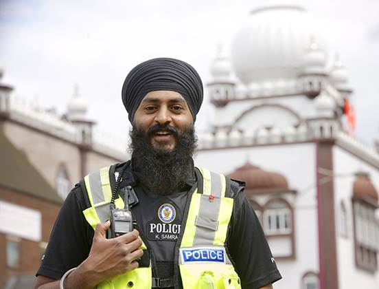 A smiling Sikh police officer with a turban and long beard