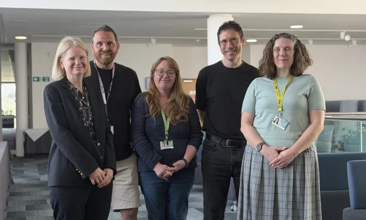 A group of people stand in an office, smiling to the camera.