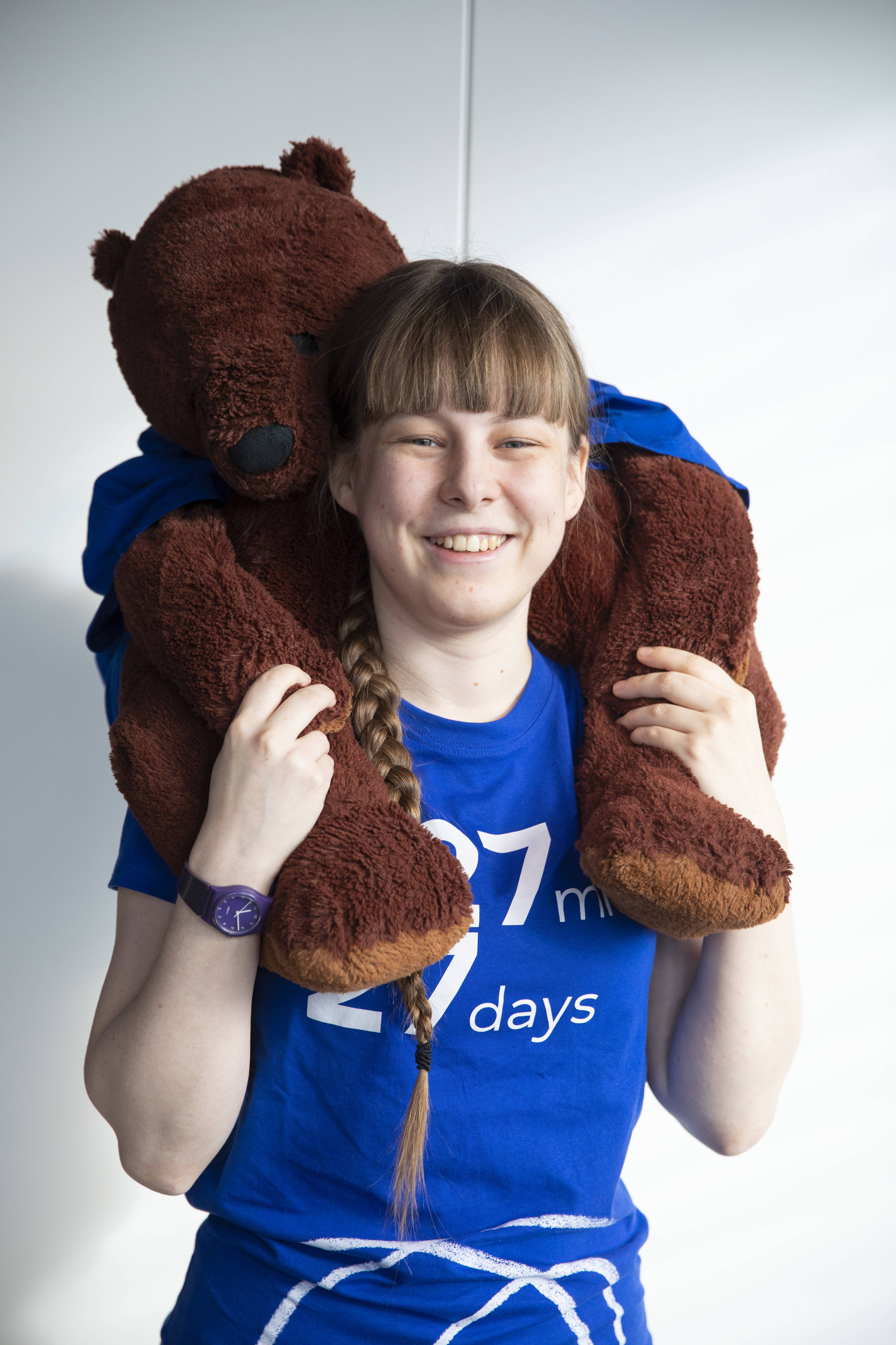 Person looking at the camera wearing a 27 27 t-shirt. They have large brown toy bear on their shoulders 