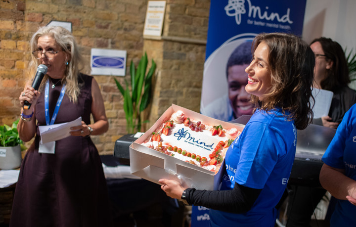 Woman Smiling at event, holding cake with Mind logo on it.